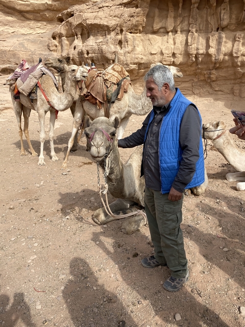 Person standing next to a resting camel in a desert area.