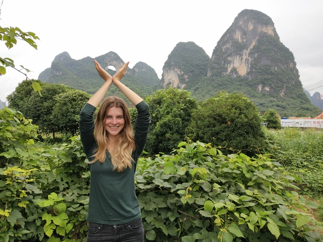 Person posing in front of karst mountains in a lush green setting.