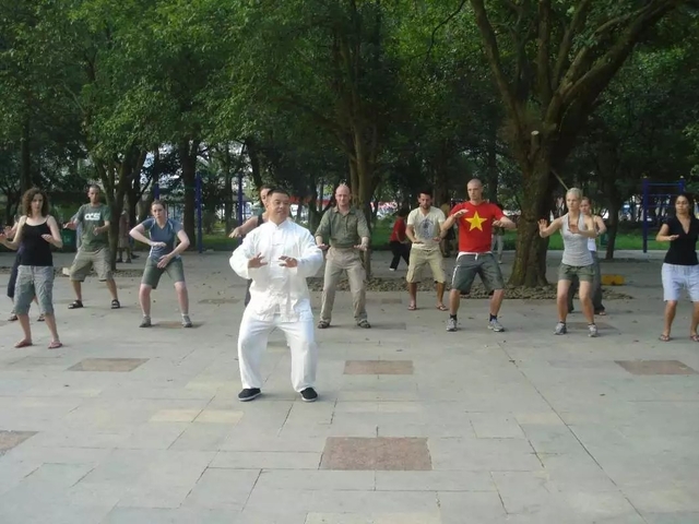 Group of people practicing Tai Chi in a park led by an instructor.