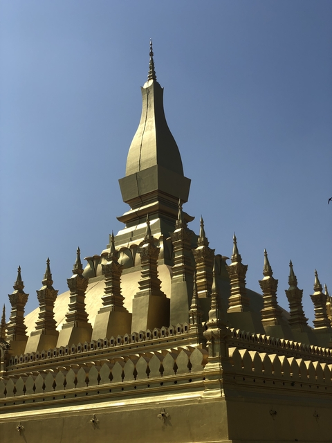       Close-up of a golden temple structure with intricate details against a clear sky.
  