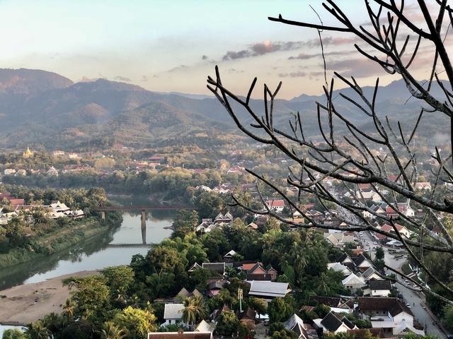       Scenic view of a river, bridge, and surrounding lush mountains at sunset.
  