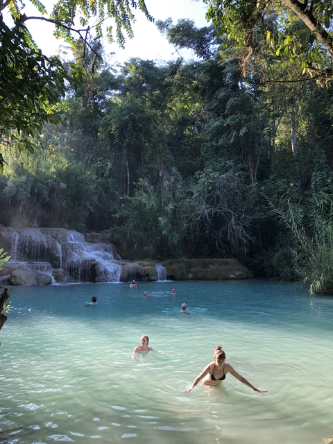       People swimming in a turquoise natural pool with waterfalls in a forest.
  