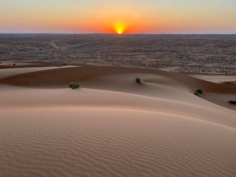 Sand dunes with a sunset in the distance.