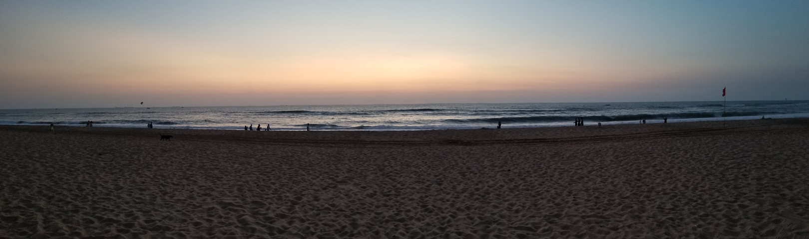 Sunset over a calm beach with people silhouetted.