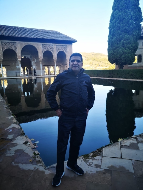 Man posing in front of a reflecting pool with palace background.