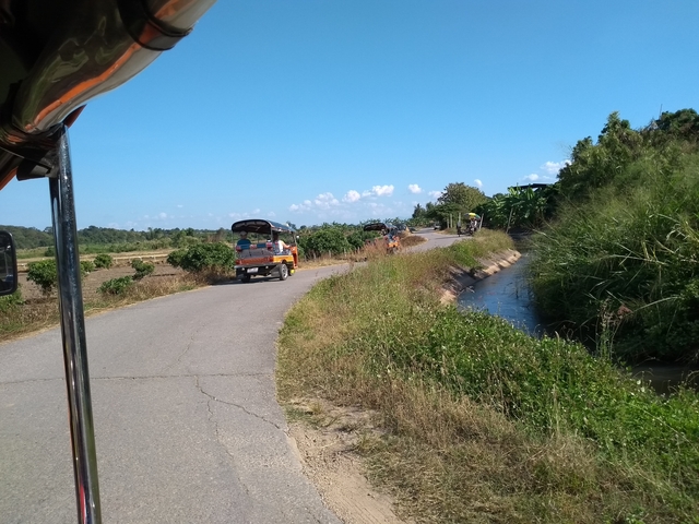 A rural road with a three-wheeled vehicle and lush greenery.