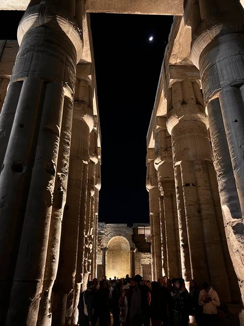       Columns and moon in a night setting with people.
  