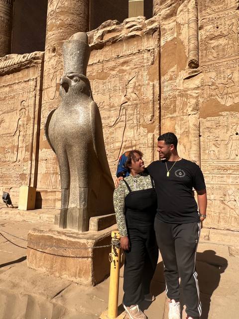       Two people standing next to an ancient statue.
  