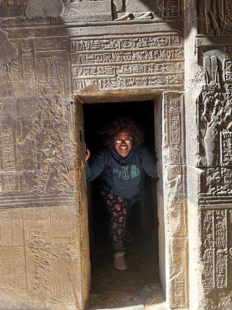       Person posing in a narrow and ornate ancient space.
  