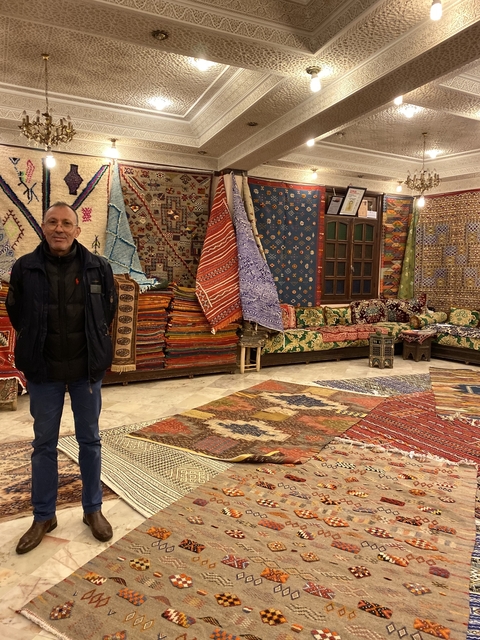       Man standing in a store filled with colorful traditional rugs.
  