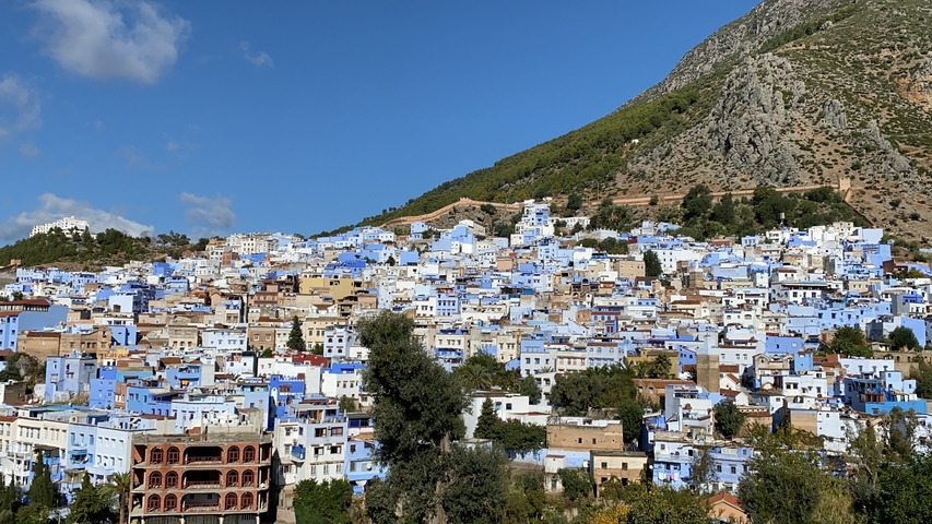       View of a city with predominantly blue buildings nestled between hills.
  