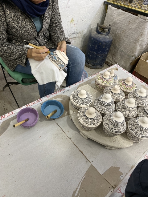       Person decorating traditional pottery with intricate designs.
  
