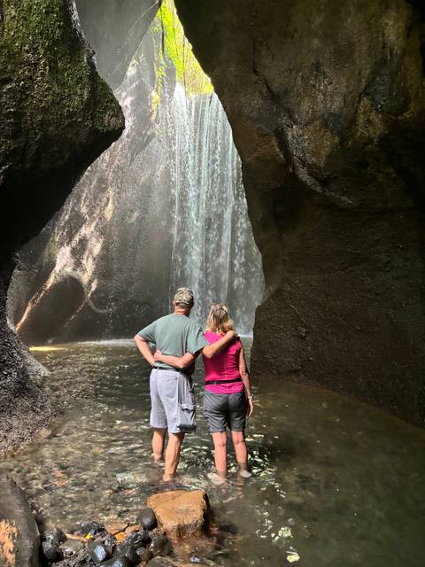 Couple standing by a waterfall inside a cave.