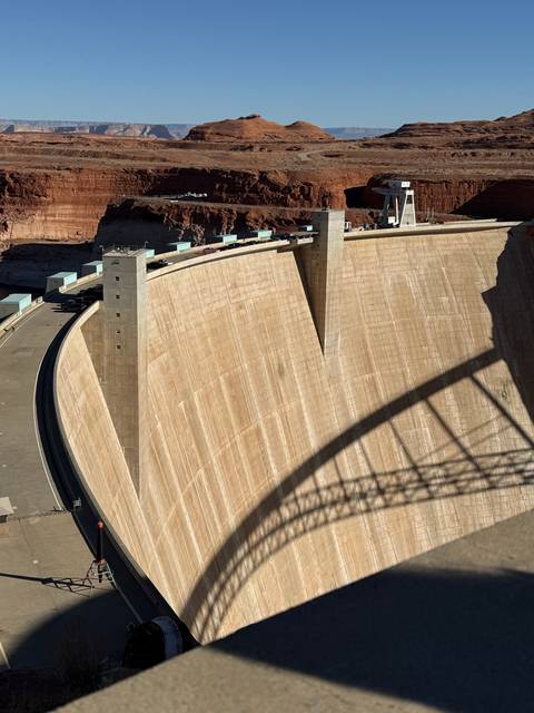 Large concrete dam with red rock formations.