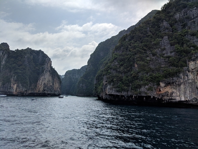 Steep cliffs enclosing a coastal cove with boats on the water.