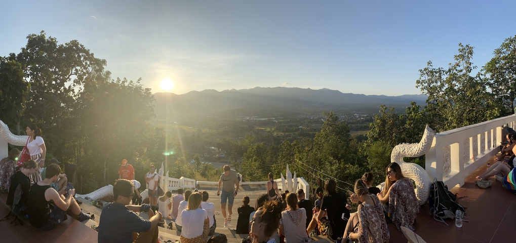 People gathered on steps watching the sunset over a valley.