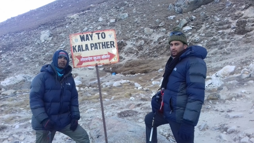       Two hikers posing beside a sign to Kala Pattar.
  
