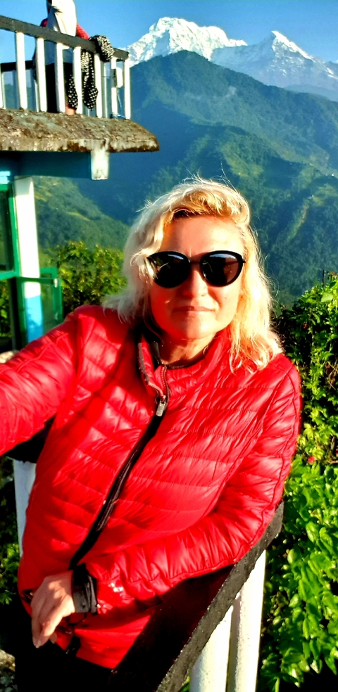 Person wearing a red jacket posing with greenery behind.