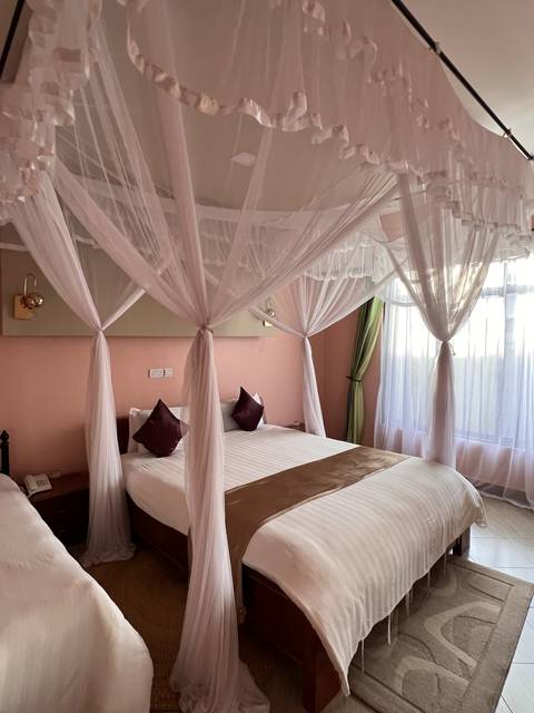       A bed with white sheets and a pink canopy in a dimly lit room.
  