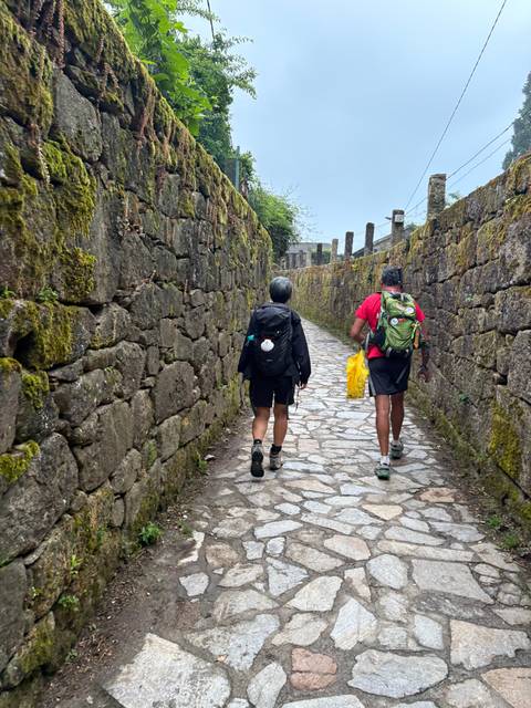 Two hikers walking along a stone pathway in the countryside.