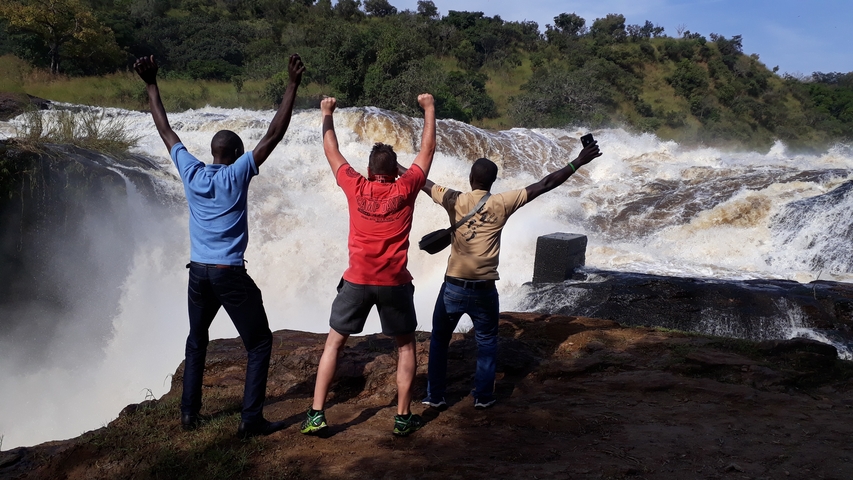Three people cheering in front of a powerful waterfall.