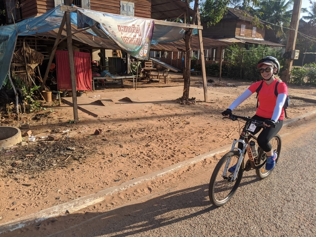 Woman cycling along a rural roadside scene.