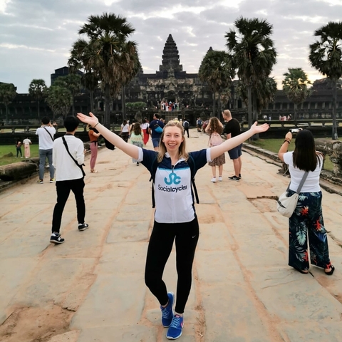 Smiling woman posing in front of historic ruins with tourists around.
