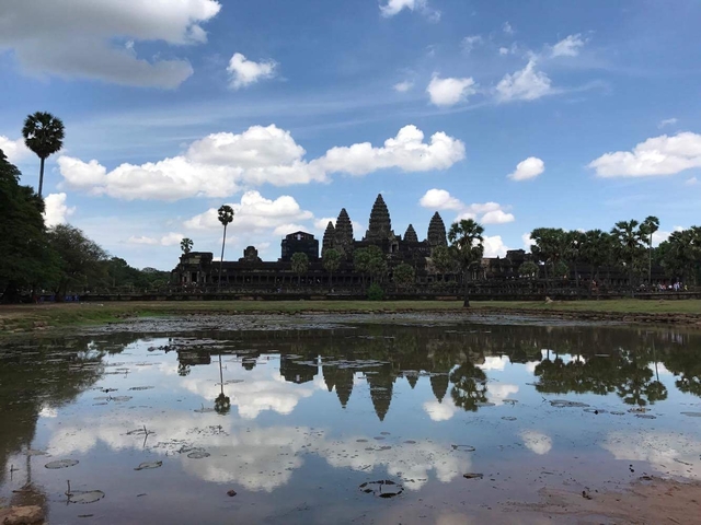       View of Angkor Wat temple reflected in a pond.
  