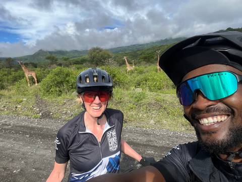 Two friends on a cycling adventure, giraffes visible in the distance.