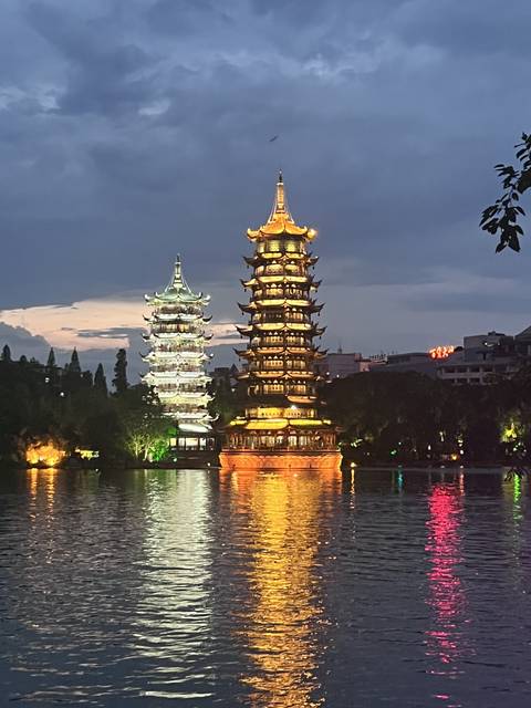 Two illuminated pagodas reflected in a body of water at dusk.