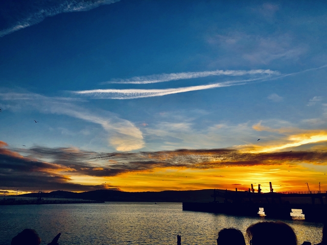 Vibrant sunset over a harbor with dramatic clouds.