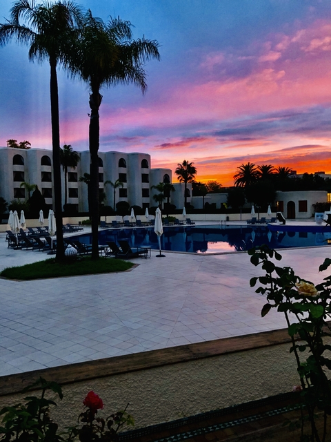 Hotel pool area during sunset with colorful sky.