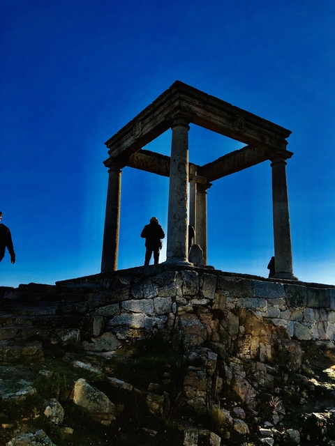 People silhouetted under an ancient stone structure.