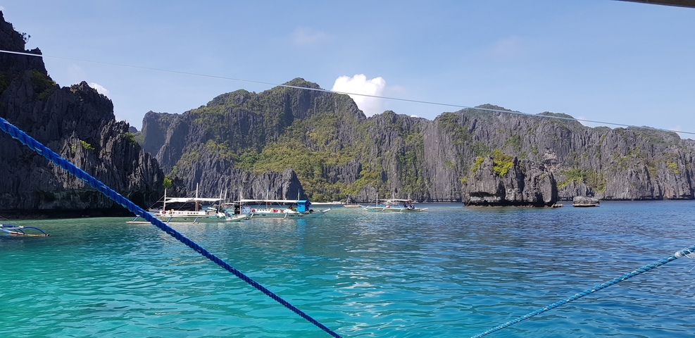       Boats on vibrant blue water with rocky cliffs.
  