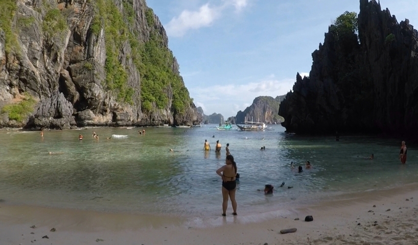       People swimming in a calm bay surrounded by cliffs.
  
