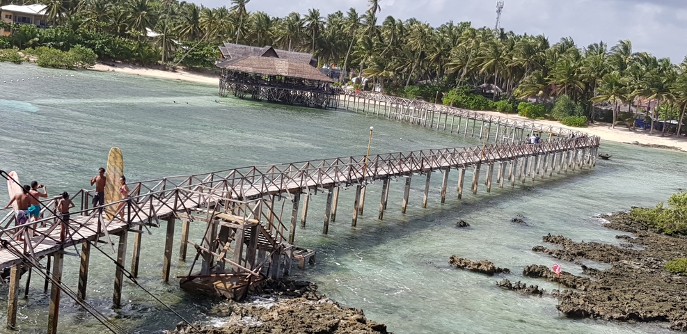       Wooden bridge over blue waters leading to a beach.
  