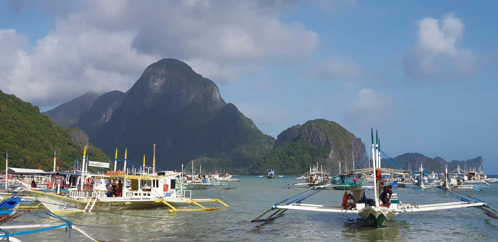       Boat-filled port with towering rock formations.
  