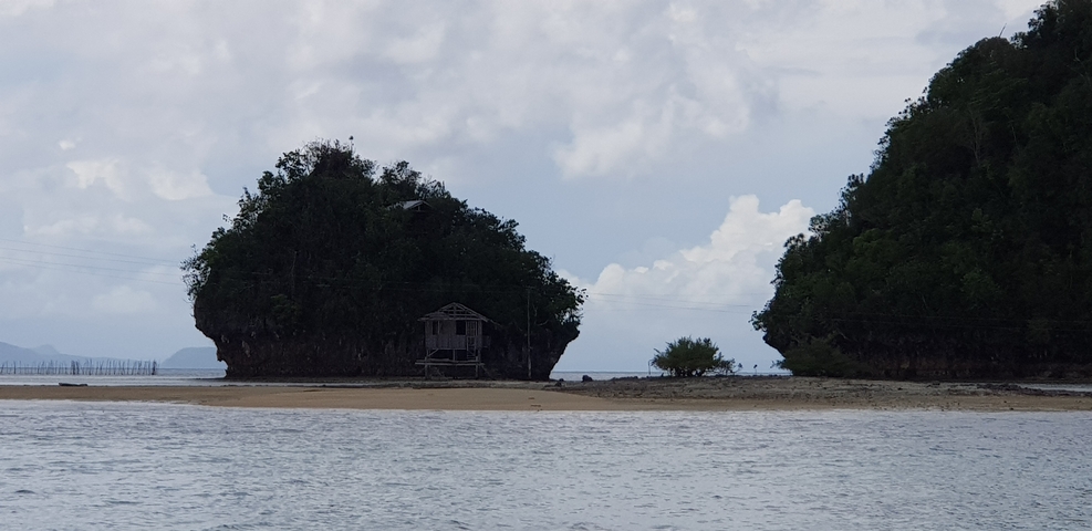      Remote house on a beach with forested rock formations.
  