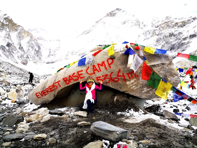       Colorful flags and a marker at Everest Base Camp in snowy surroundings.
  