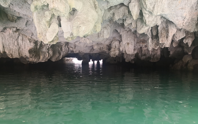 Inside a cave with stalactites reflected in the water.