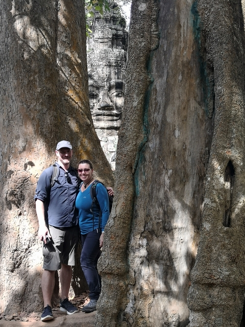 Couple posing next to large tree roots.