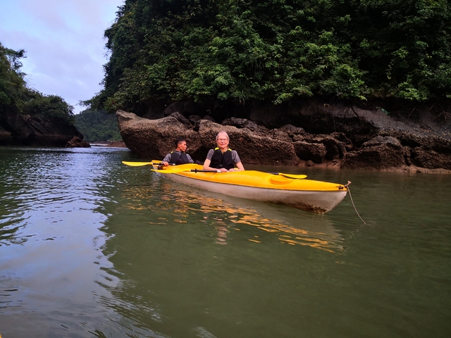       Two people kayaking on calm water near rocks.
  