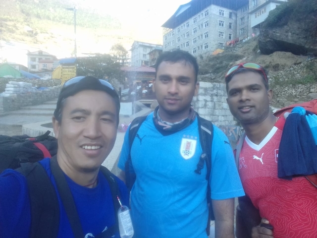       Three people posing in an outdoor setting with buildings in the background.
  