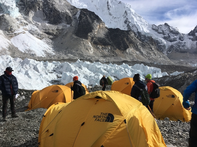       Camping tents and people at the base of a snowy mountain range.
  