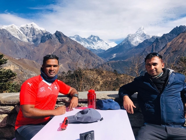       Two people sitting at an outdoor table with Himalayan mountains in the background.
  