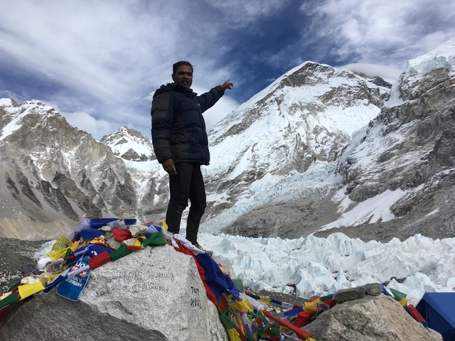       Person pointing towards a snowy mountain peak with a glacier in the background.
  