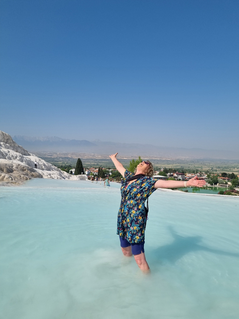       Person joyfully posing in front of the travertine terraces with a scenic view.
  