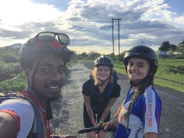       Three cyclists posing on a road with scenic views.
  