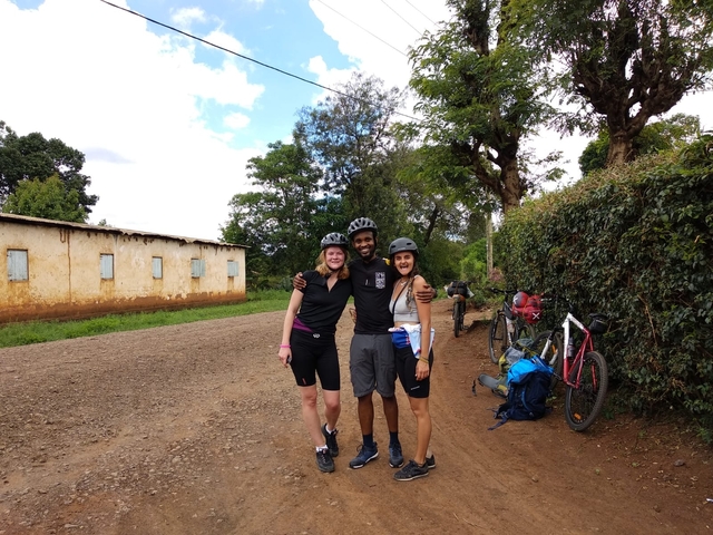       Three people posing with bicycles on a dirt road.
  