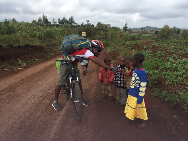       Cyclist handing something to children on a road.
  